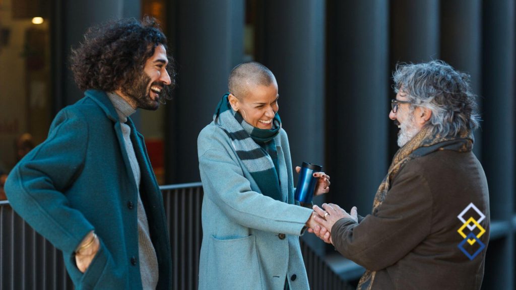 Three people talking outside an office building, two of them shaking hands