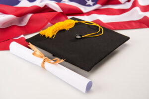 A graduation cap and diploma with an American flag backdrop, representing the achievements enabled by education scolarship.