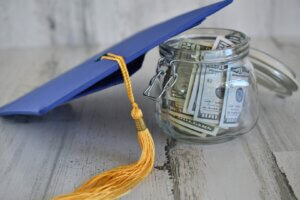 A university graduation cap placed beside a glass jar filled with money, symbolizing the financial support of scholarships for education. The scene represents the concept of scholarship requirements by visually associating the cost of education with academic achievement.