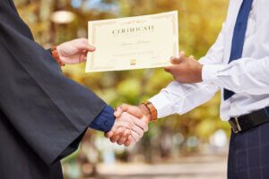 A close-up view of a hand presenting a diploma to another, symbolizing the culmination of hard work and the vital support provided by scholarship trust initiatives.