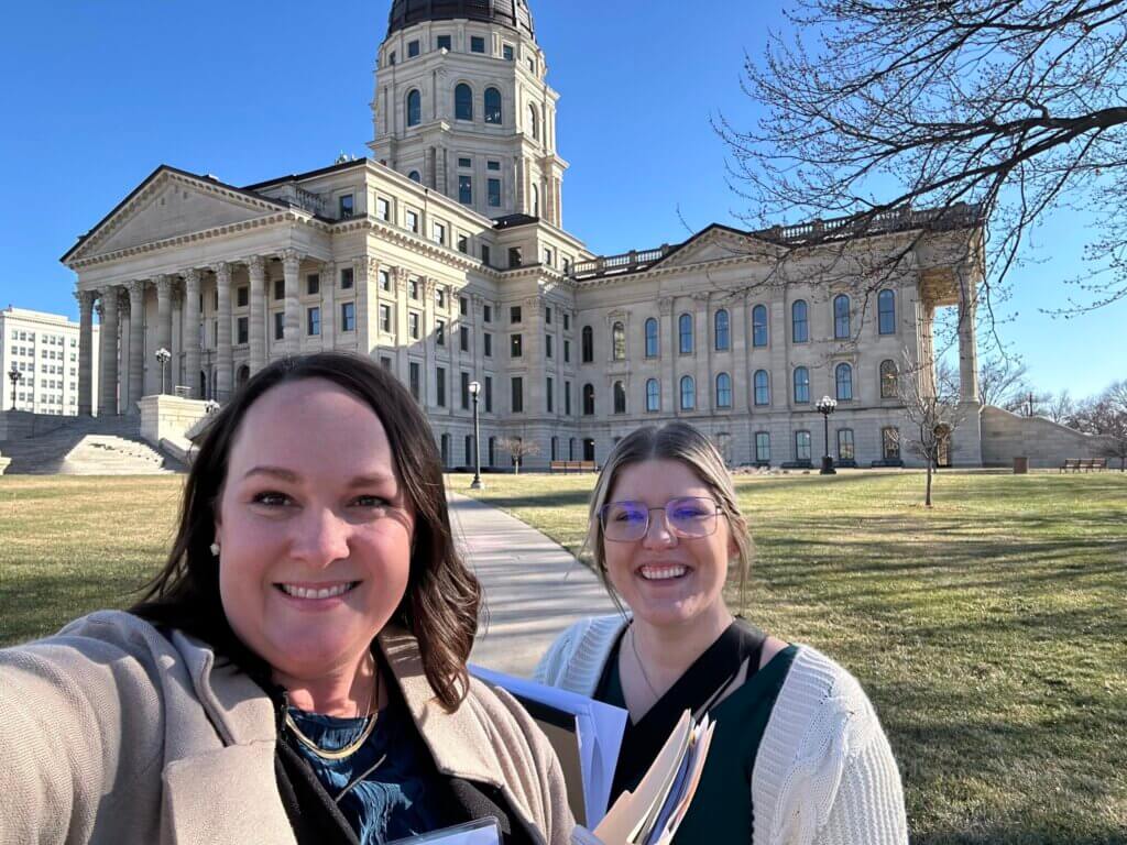 Two women standing in front of the Kansas State Capitol in Topeka