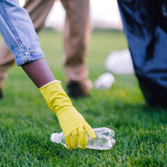 A person in work gloves picking up litter from grass