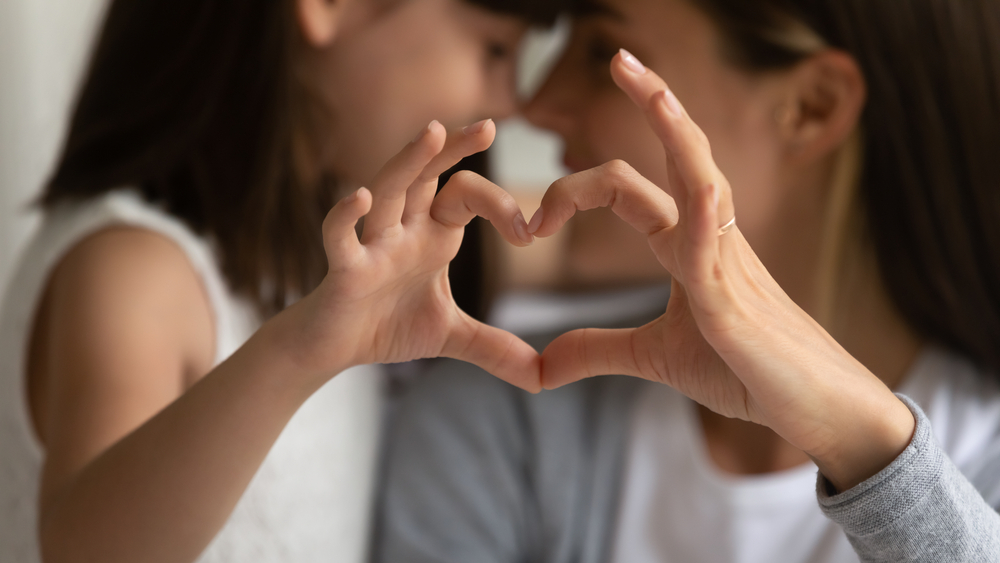Mother and child making a heart shape with their hands, symbolizing love, compassion, and giving, reflecting the question of how much does the average person donate to charity.