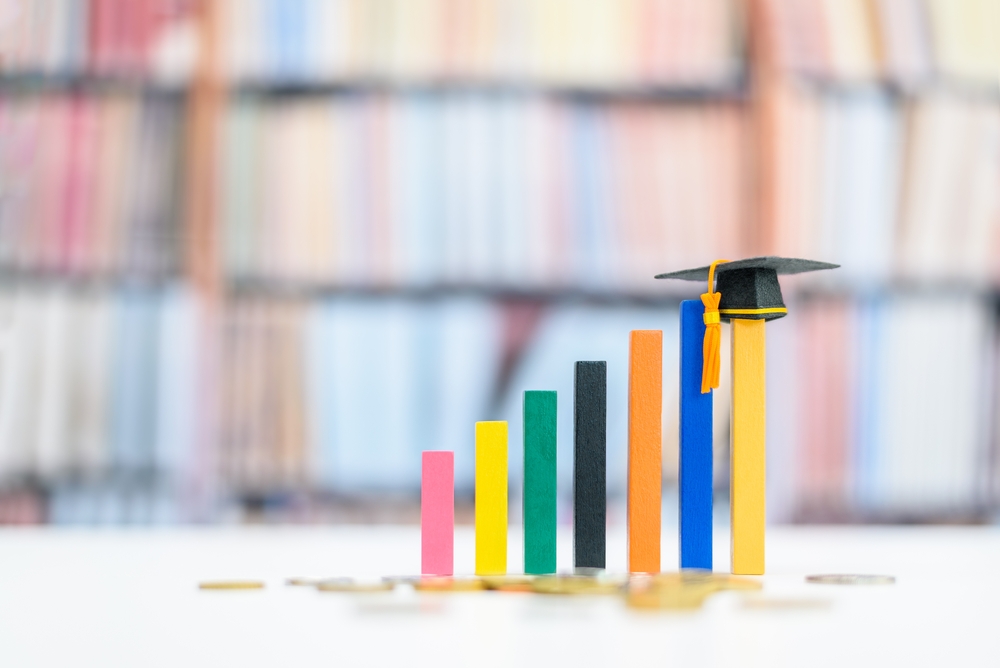 Colorful bar chart blocks arranged in ascending order, with the tallest block wearing a graduation cap, symbolizing growth and education success, representing charitable donation to public causes in education.