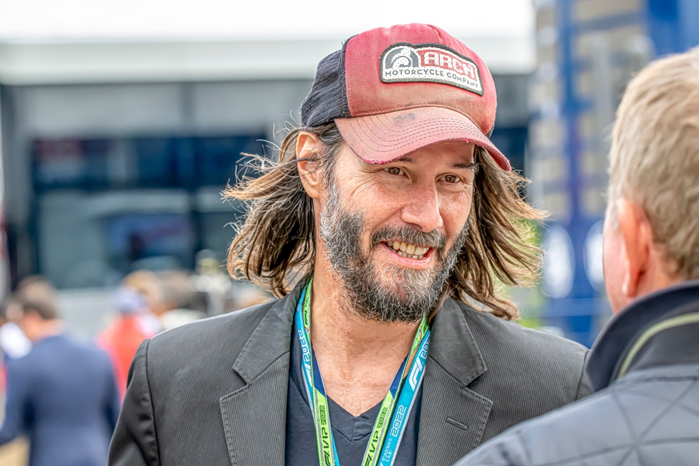 Actor Keanu Reeves smiles while speaking with someone at an outdoor event, often cited among generous celebrities for his low-key but consistent philanthropic actions.