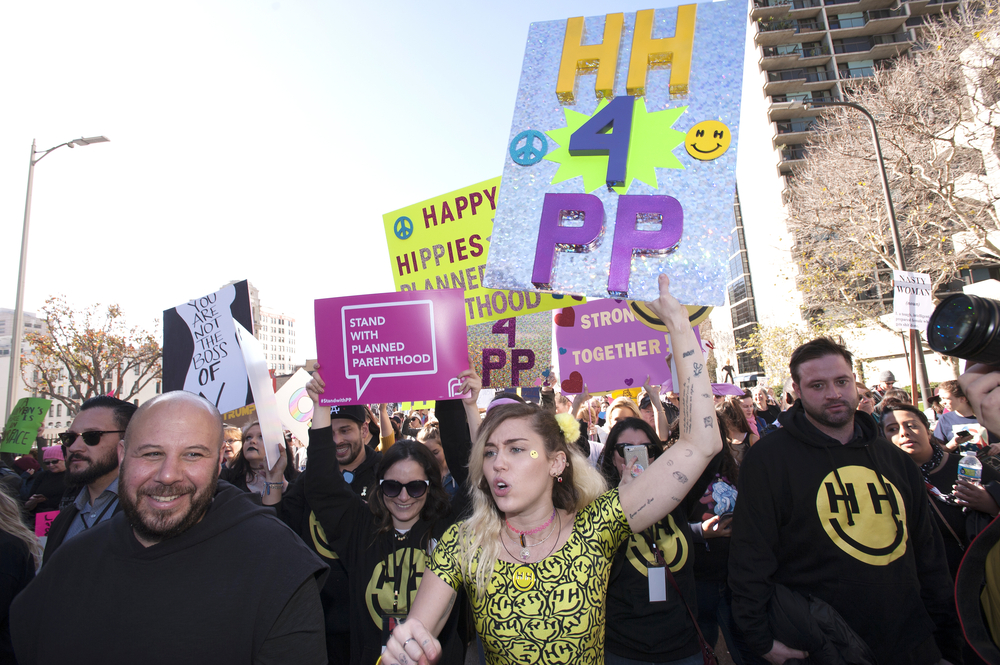 A crowd of demonstrators, including Miley Cyrus, march while holding signs in support of Planned Parenthood, illustrating how celebrity activism often highlights what charities do celebrities support.