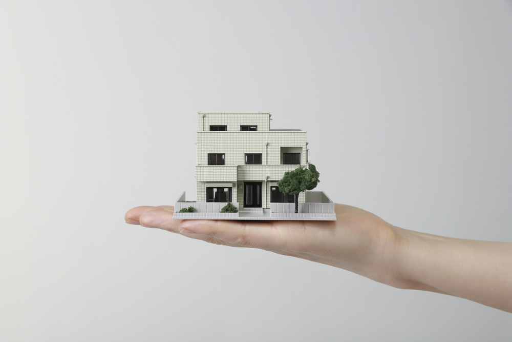 Real estate donations concept: a hand holding a miniature modern house, symbolizing property gifting or charitable real estate contributions.