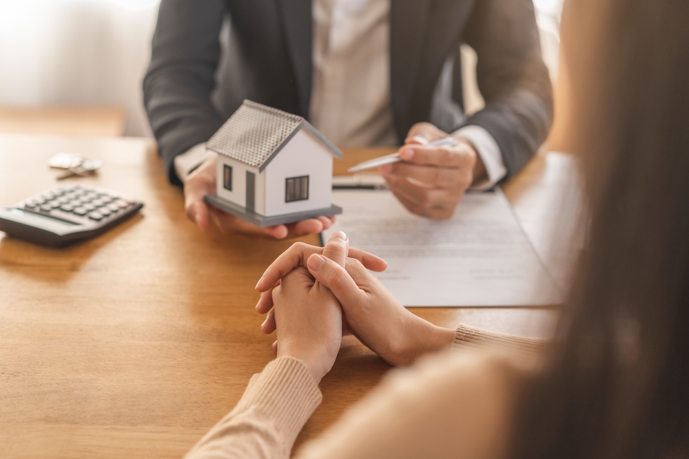 What charities accept real estate donations concept: a client meeting with a professional, reviewing documents while a house model and keys are presented, symbolizing guidance on which organizations accept property donations.
