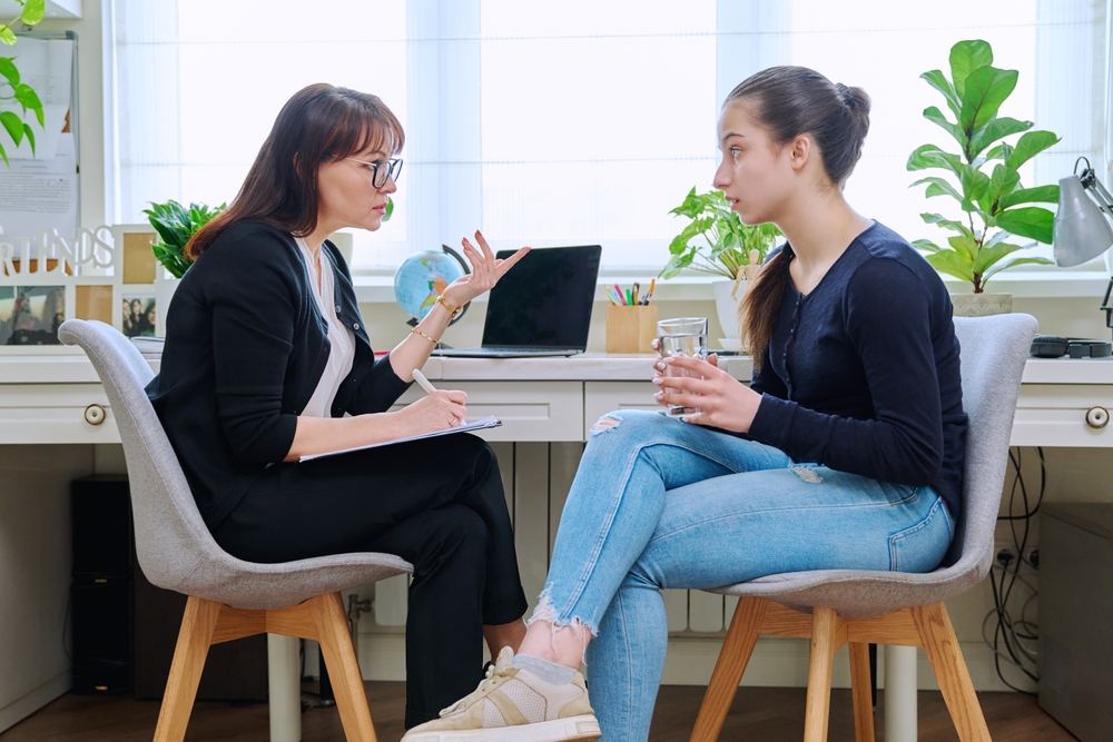 A high school student talks with a school counselor at a desk in a bright office