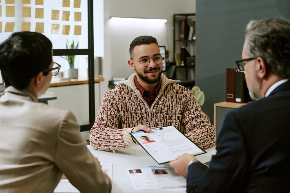 Young man in casual clothes talking with two older adults over printed documents at a table