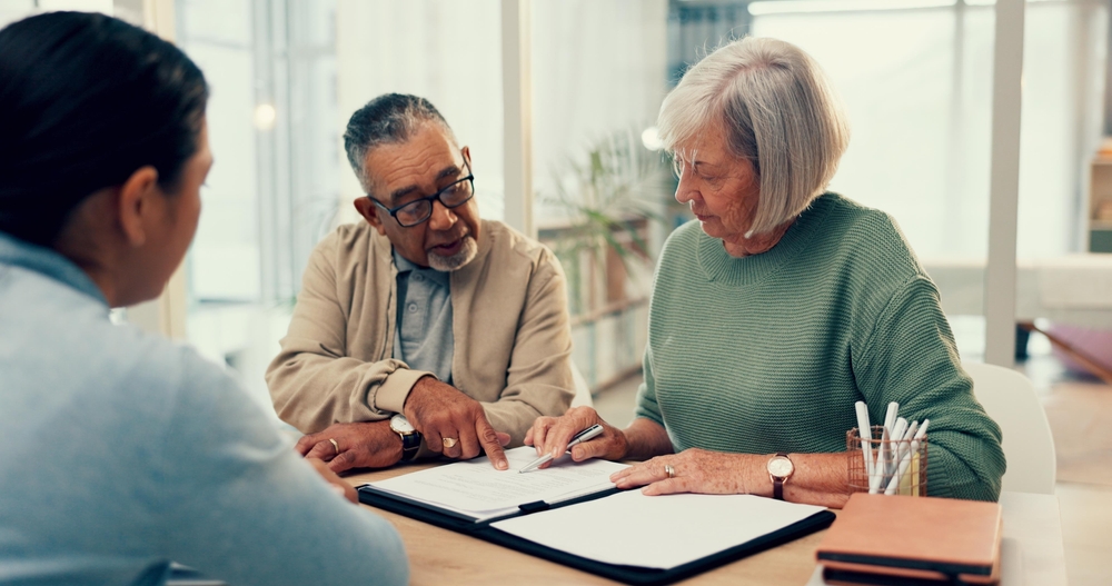 An older couple reviews documents with an adviser across a table in an office