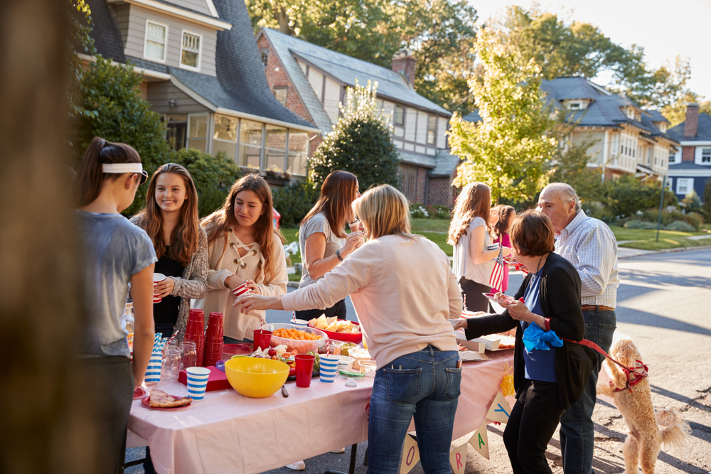 Neighbours gather around a food table set up on a residential street at a block party
