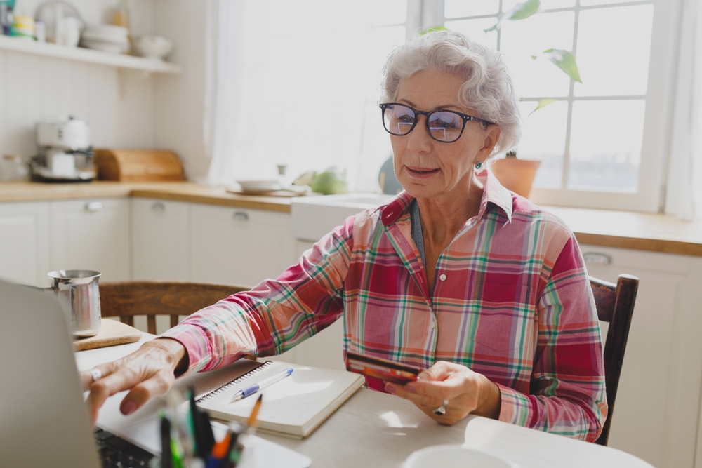 Older woman making an online payment on a laptop at her kitchen table