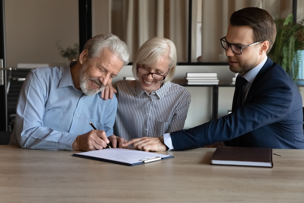 Couple signing paperwork at a desk while an adviser sits across from them in an office