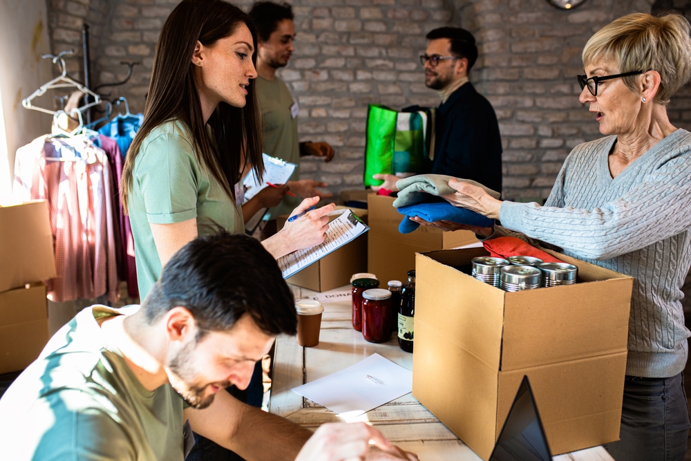Volunteers of different ages sort donated clothing and food into boxes at a charity centre