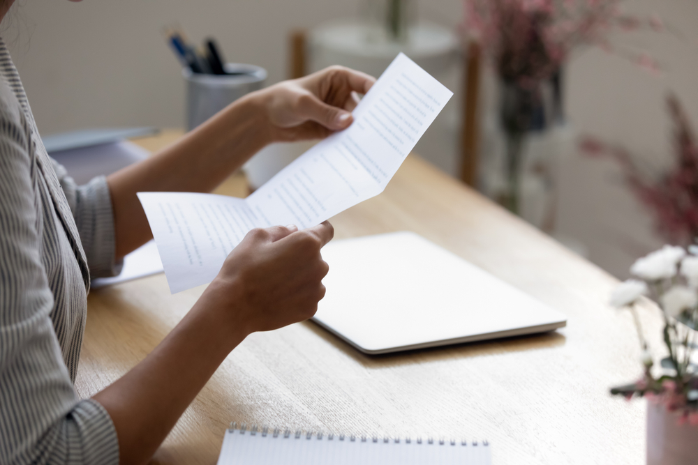 Person reviewing a printed document beside a laptop and notebook, illustrating a grant proposal sample.