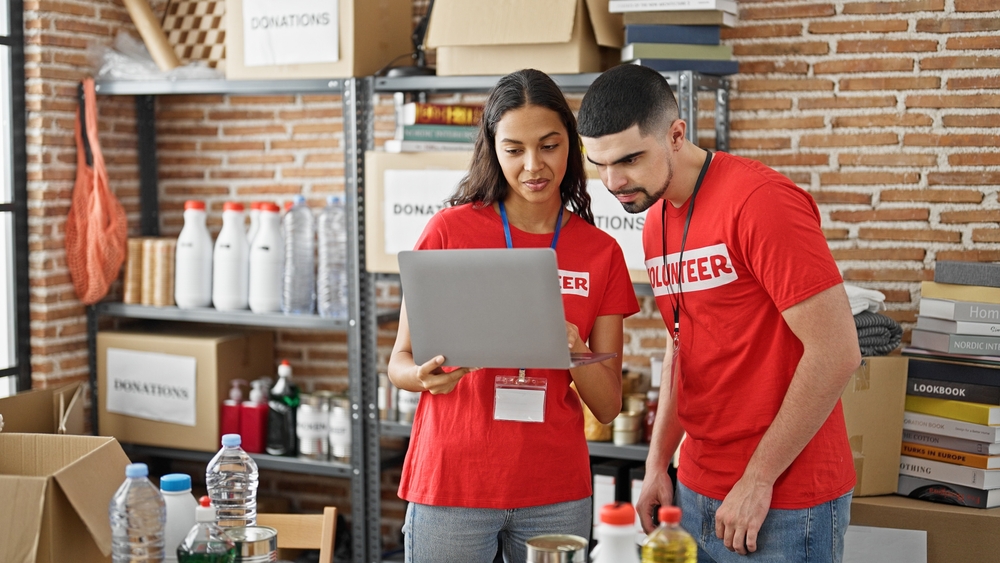 volunteers using a laptop while organizing donated goods, illustrating fundraisers for nonprofits through coordinated donation drives, community campaigns and volunteer support.