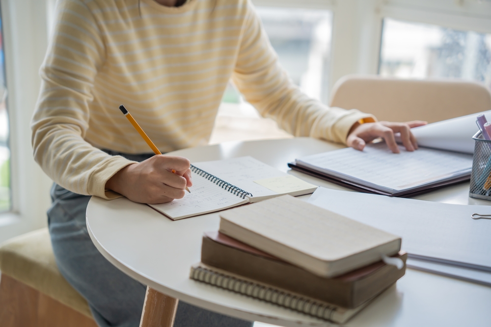 Student writing notes beside books and study materials, illustrating Scholarship Essay Examples for academic applications and personal statements.
