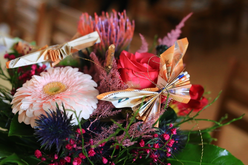 Colorful flower bouquet decorated with folded cash, illustrating the in lieu of flowers meaning as a request for donations or another tribute instead of floral arrangements.