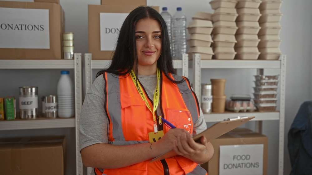 Volunteer wearing a safety vest holding a clipboard in a food donation center, representing an employee volunteer program.