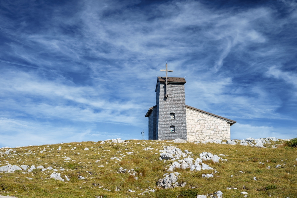 Small church fundraising ideas for a rural congregation, featuring a small stone church on a peaceful hillside under a bright blue sky.