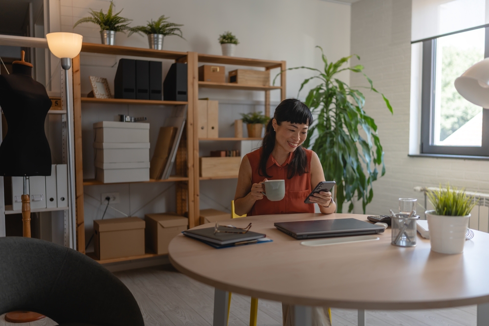Professional at a desk using a smartphone during a break, representing flexible employee volunteering and workplace participation.
