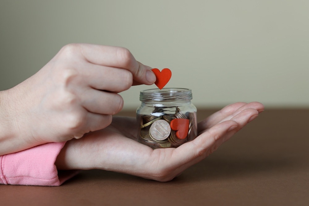 Hands placing a heart into a jar of coins, illustrating donor restricted funds designated for a specific charitable purpose.
