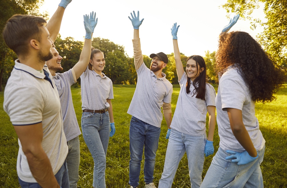 Group of volunteers raising their hands together in a park, illustrating Community Essay Examples focused on service, teamwork, and local involvement.