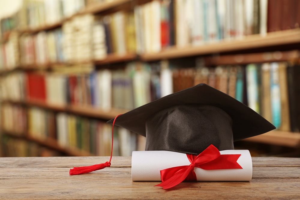College scholarships for high school seniors, featuring a graduation cap and diploma on a table with library books in the background.