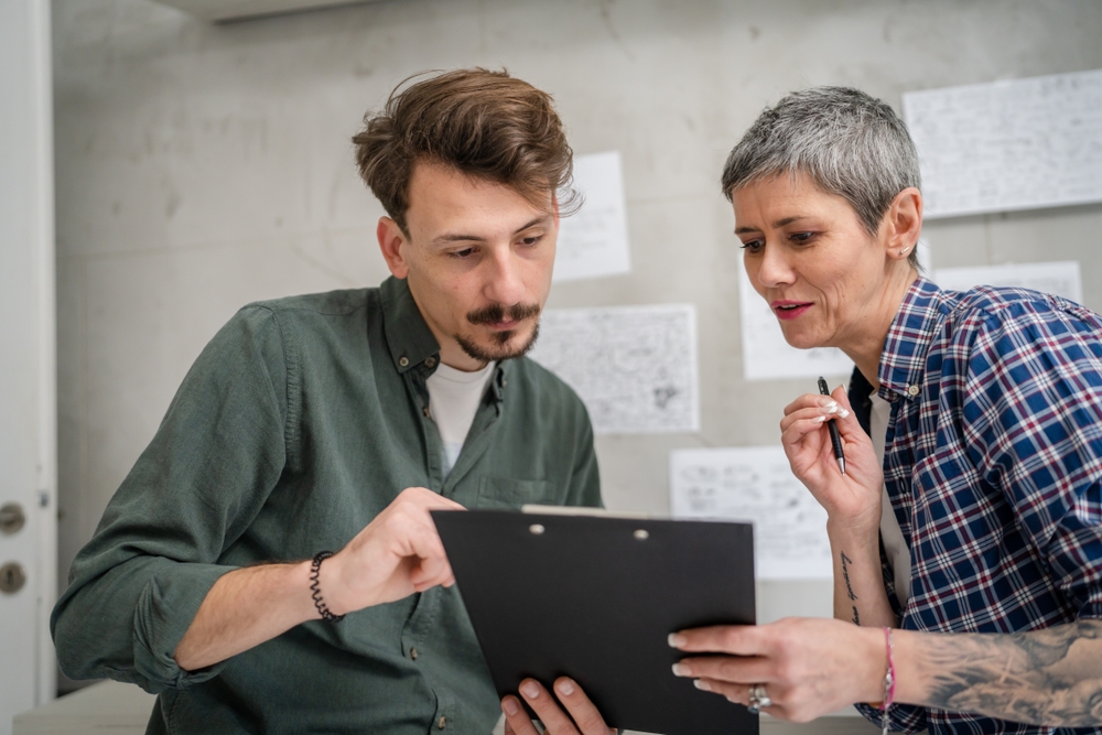 Two people reviewing paperwork on a clipboard together in a plain workroom