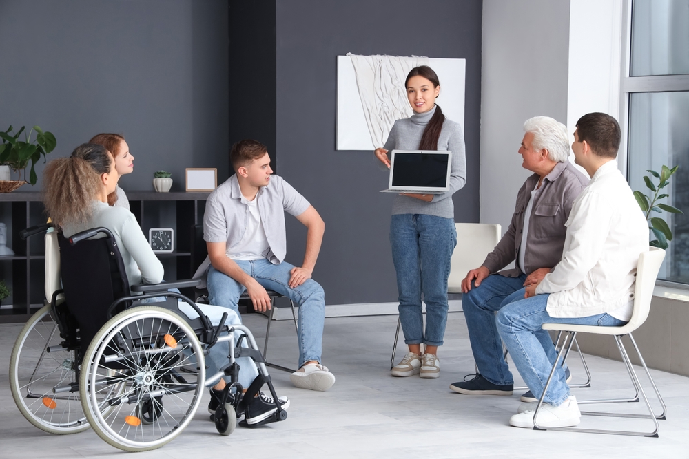 Woman shows a laptop to a small group seated in chairs in a plain community room