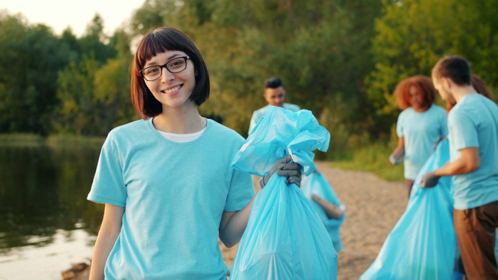 Smiling young volunteer holding a full trash bag during a lakeside cleanup, one of many community service opportunities near me for students.