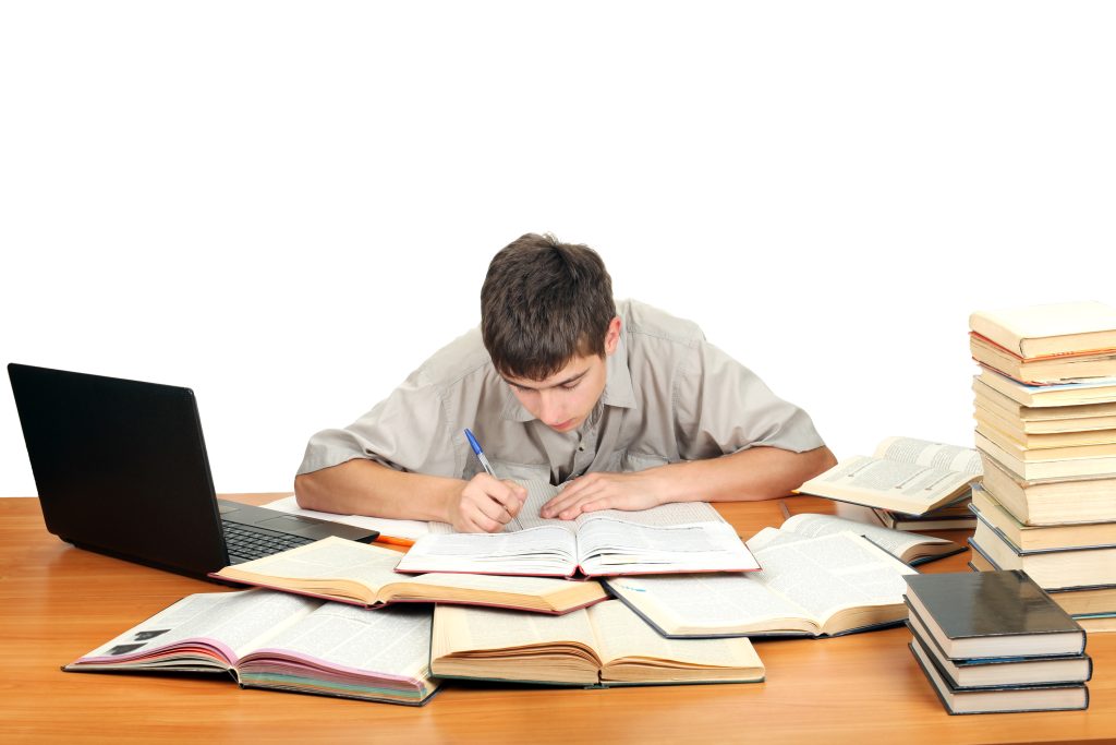 Student bent over a desk writing in a notebook, working out how to make a scholarship essay one step at a time.