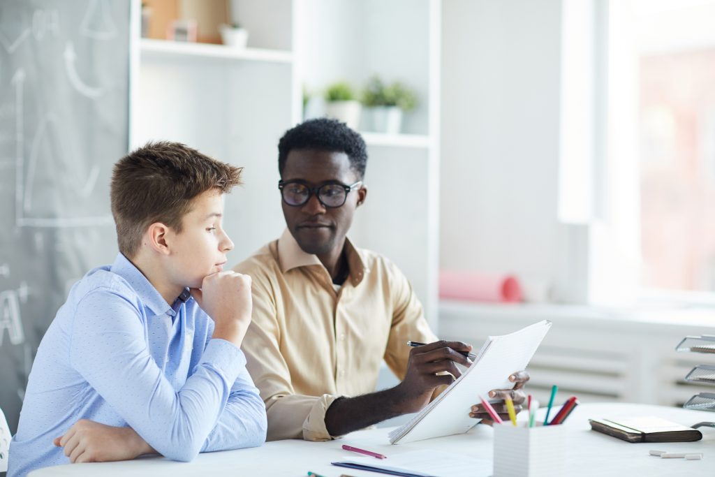 Teacher pointing at a page of a student’s essay while he explains it, practicing how to end a scholarship essay.