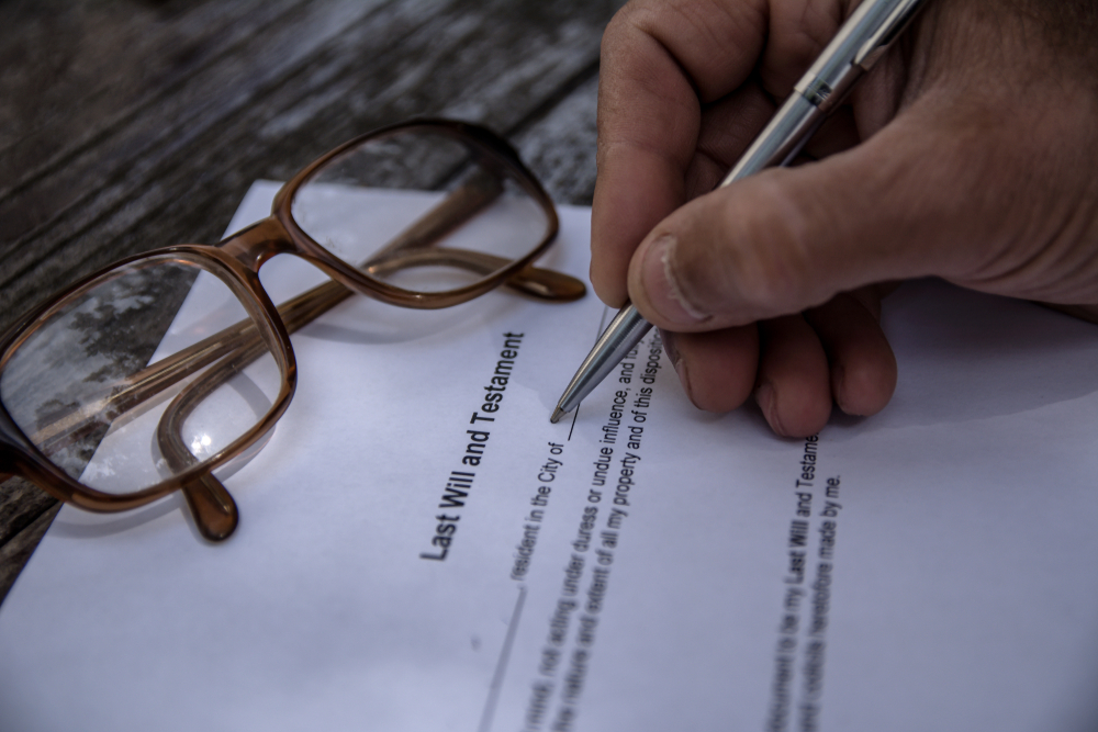 An older man signing his last will and testament at a table, the moment a charitable bequest is put in writing.